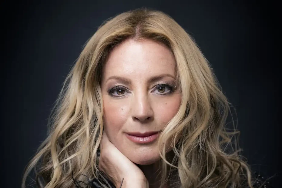 Close up headshot of Sarah McLachlan. She rests her hand on her chin in front of a dark black background.